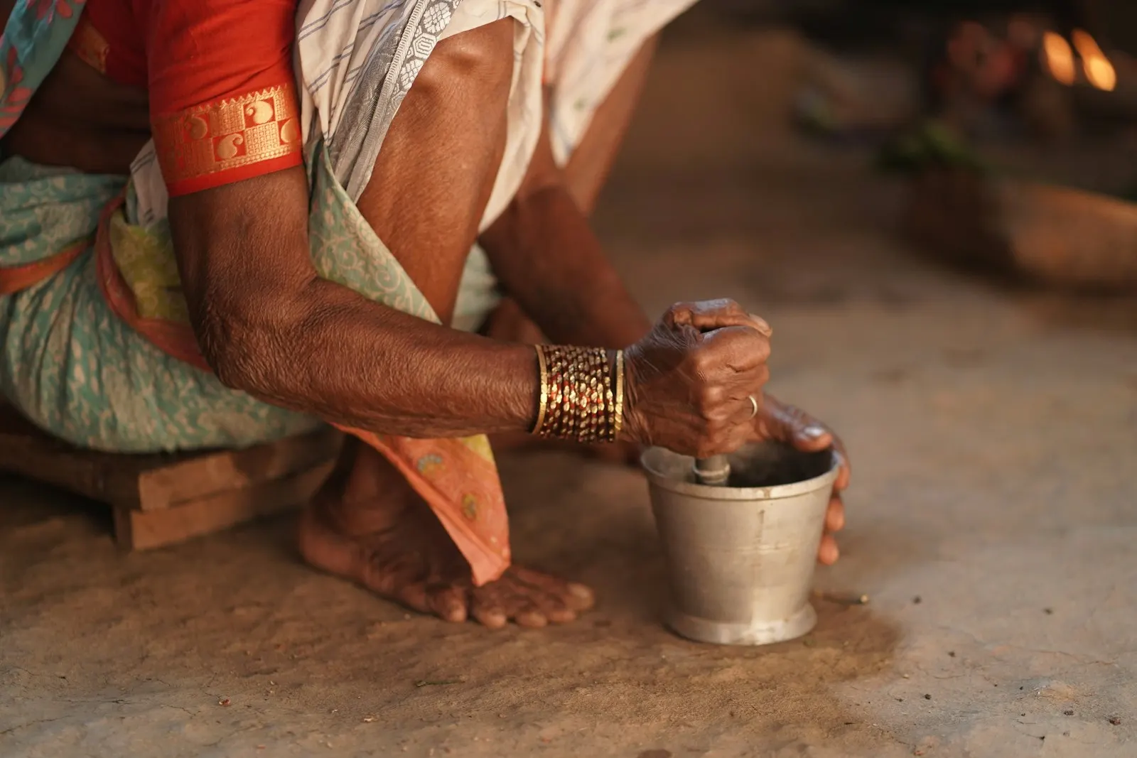 Weathered hands grinding fresh spices in a small metal mortar by candlelight