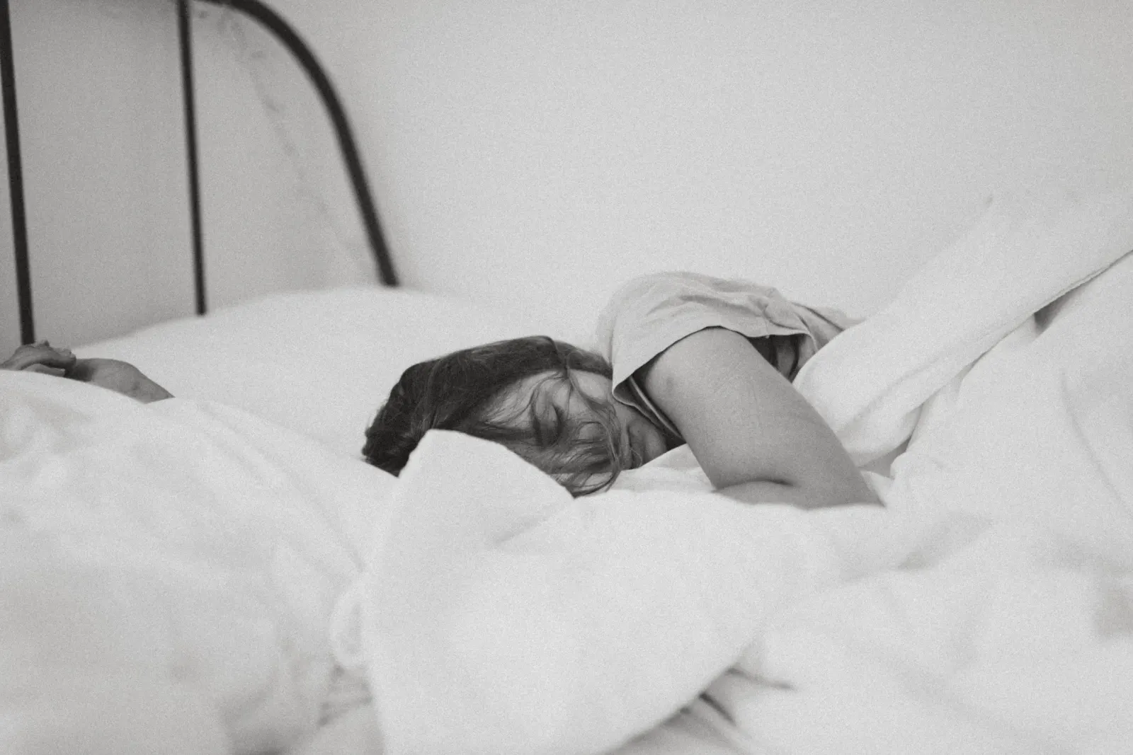 Person resting in soft white bedding, head turned to one side in deep sleep