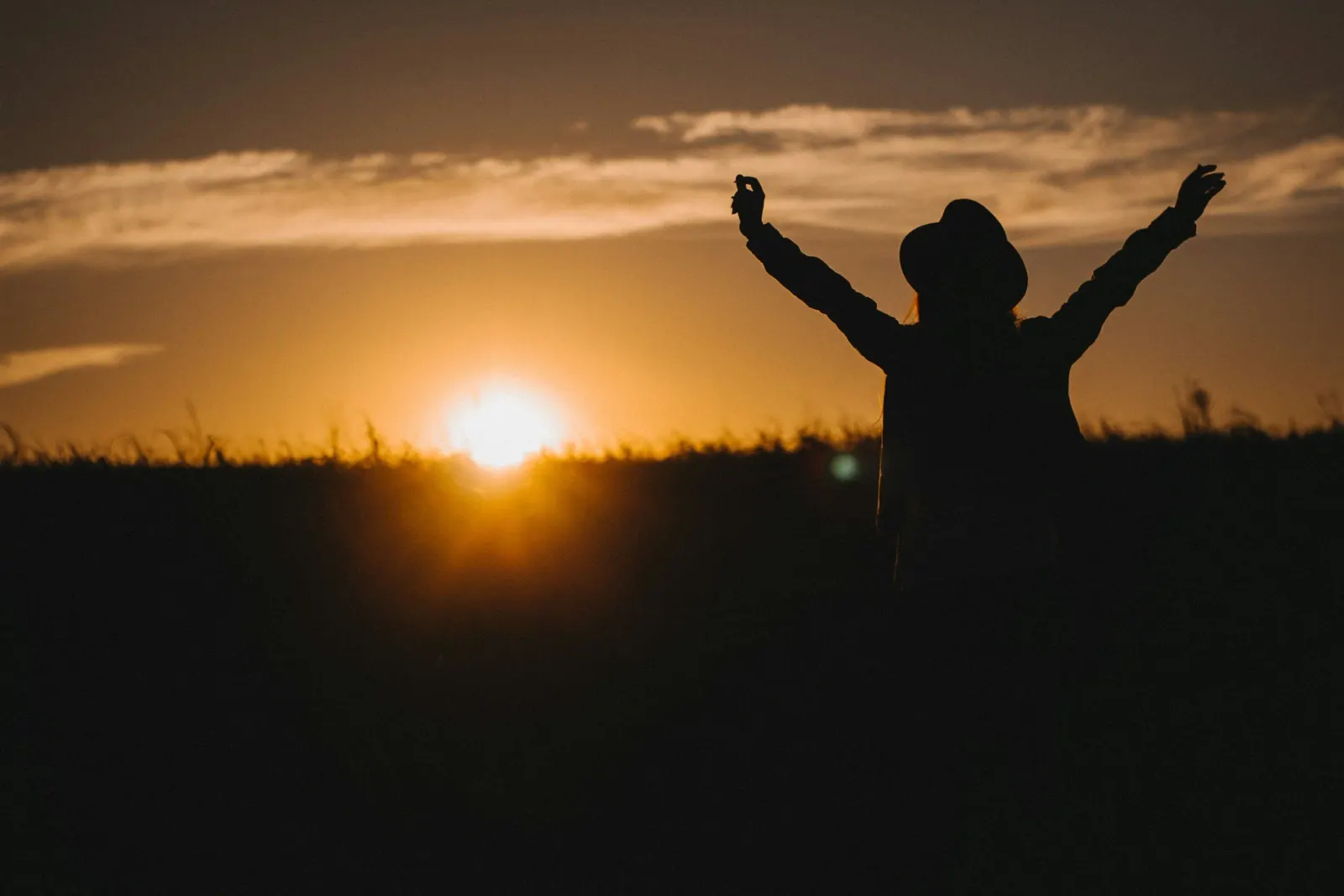 Silhouette einer Person mit erhobenen Armen vor einem warmen Sonnenaufgang